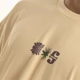 Remera color beige de corte holgado con estampado pequeño en el pecho de una flor y la letra S.