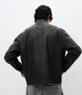 Campera estilo racing confeccionada en poliuretano, con diseño bicolor en negro y beige. Presenta cuello alto con botón a presión, cierre frontal metálico, panel frontal contrastante y franjas laterales deportivas.
