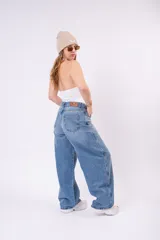 Pantalón de jean wide leg en lavado azul claro vintage, con corte amplio y fluido. Presenta un cierre asimétrico con botones expuestos en la parte delantera, talle alto y bolsillos funcionales.