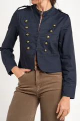 Chaqueta corta color beige de algodón, de inspiración militar con cuello mao y doble botonadura frontal con botones metálicos dorados.