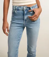 Pantalón bootcut de tiro alto en denim azul claro, ceñido en caderas y muslos con corte acampanado hacia el bajo y detalle de pequeña abertura lateral en los tobillos. Cuenta con bolsillos y cierre tradicional con botón y cremallera.