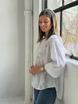 Camisa blanca de corte holgado y manga larga, con delicados bordados florales en tono gris claro en el frente.