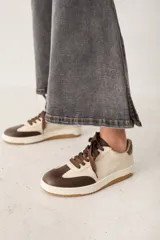 Zapatillas urbanas de cuero con diseño bicolor en tonos crema y marrón. Presentan cordones marrones, suela de goma con textura y detalle de marca en el lateral.