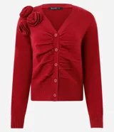 Cardigan de punto color rojo con escote en V y cierre frontal de botones. Presenta un diseño con pliegues frontales que aportan textura y aplicaciones de flores en relieve en uno de los hombros.