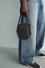 Bandolera vertical negra con acabado engomado, compartimento principal con cierre de cremallera y bolsillo interior plano. Bolsillo frontal con cierre de cremallera. Asa de hombro ajustable y extraíble.