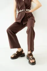 Cinturón negro de cuero charol con hebilla metálica plateada y ojales metálicos.