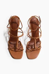 Sandalias de taco alto con tiras finas, color suela, punta cuadrada y diseño con nudo decorativo delantero. Tienen pulsera ajustable con hebilla en el tobillo y taco cuadrado.