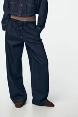 Pantalón de jean de tiro alto con corte de pierna ancha, cintura elástica con cordón ajustable y bolsillos laterales.