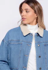 Campera de jean celeste con cuello y forro de corderito color crema, corte cuadrado, cierre frontal con botones metálicos, dos bolsillos de parche en el pecho y elástico en el ruedo.