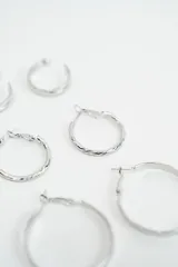 Set de tres pares de aros tipo argolla en color plateado, con diferentes texturas y tamaños, incluyendo un par liso pequeño, un par con textura trenzada mediano y un par liso grande.