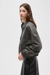 Campera de estilo utilitario en color gris oscuro con efecto lavado, confeccionada en poliéster. Presenta cuello camisero, cierre frontal con cremallera, bolsillos frontales con solapa y puños elásticos.