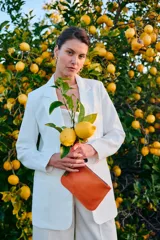Sobre de cuero color naranja con diseño clásico, cierre metálico superior y correa de mano lateral.