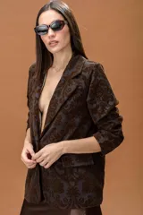Blazer de corte estructurado confeccionado en tejido jacquard con estampado ornamental en tonos marrones. Presenta solapas clásicas, cierre frontal y diseño de manga larga.
