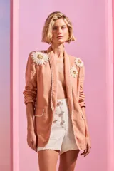 Blazer de lino color salmón con solapas pronunciadas, bolsillos delanteros ribeteados y mangas largas. Cuenta con apliques florales de crochet en los hombros y detalles de ribete blanco en solapas y bolsillos.