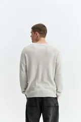 Sweater oversize de tejido liviano color gris claro, con hombros caídos, cuello redondo, costuras a la vista y bordado sutil en el pecho.
