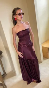 Vestido largo strapless de lamé elastizado color bordó, con cuerpo fruncido tipo corsel y falda larga amplia con volados y frunces.