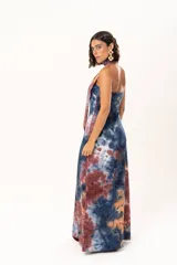 Vestido largo de escote recto sin mangas, confeccionado en tela con estampado batik en tonos azul, naranja y bordó. Presenta un diseño ajustado con tajos laterales y un lazo largo a juego que se puede usar anudado al cuello.
