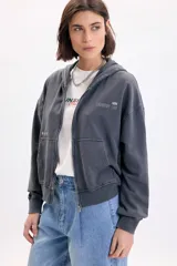 Campera deportiva con capucha y cierre frontal, de color gris con efecto acid wash. Presenta bolsillos tipo canguro, estampa con la inscripción 'Creative Lab' y detalles de pequeñas estrellas en el pecho.