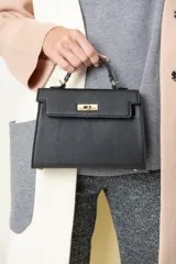 Cartera negra de imitación cuero con asa corta y correa larga desmontable. Tiene broches metalizados dorados, bolsillo interior y cierre de seguridad.