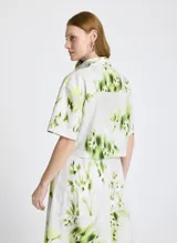 Camisa corta de mangas cortas con estampado abstracto en tonos verde y amarillo sobre fondo blanco.