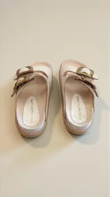 Sandalias planas de cuero color blanco, con dos tiras anchas ajustables mediante hebillas metálicas doradas y detalles pintados a mano en tonos multicolores.