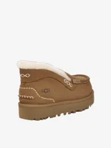 Mule de gamuza color tostado con forro de piel de oveja visible en el borde superior. Presenta costuras decorativas en contraste y una suela de plataforma dentada de goma.