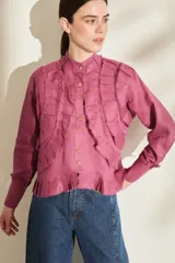 Camisa de lino color morado, con cuello mao, cierre frontal con botones y mangas largas con puños estructurados. Presenta detalles de volados frontales y ruedo con terminaciones desflecadas.