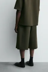 Bermuda de corte oversized confeccionada en tejido técnico compacto con elasticidad. Presenta cintura elástica ajustable con cordón, pinzas en el delantero y la espalda, y bolsillos laterales.