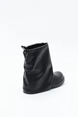 Bota de caña baja color negro, confeccionada en poliuretano con acabado liso y estructura flexible que genera un efecto fruncido. Presenta puntera redondeada, base baja y un cierre metálico en la parte trasera de la caña.