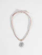 Collar con cordón de tela en estampado de cuadros vichy rosa y beige, adornado con pequeñas cuentas metálicas y un dije central de sol en color plateado.