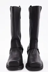 Bota de caña alta estilo western confeccionada en cuero vacuno negro. Presenta un diseño robusto con taco cuadrado de madera, punta redondeada y una tira decorativa con herrajes metálicos y tachas en la zona del tobillo.