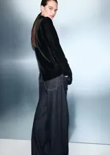 Blazer de terciopelo negro con cuello de solapa, cierre frontal cruzado con botones y bolsillos laterales con solapa. Presenta un diseño recto con forro interior y mangas largas con puños abotonados.