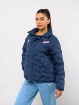 Campera puffer corta de Umbro para el Club Nacional de Football, color azul marino con diseño termosellado. Cuenta con cuello alto, cierre frontal con botones a presión, bolsillos laterales y logo de la marca junto al escudo del club en el pecho.