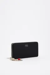 Billetera Bimba Y Lola de color negro con cierre perimetral de cremallera metálica. Cuenta con el logotipo impreso en plateado en el frente y tirador de cordón marinero con detalles en rojo.
