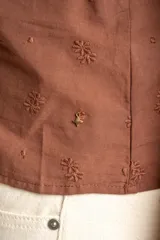 Blusa marrón de algodón con bordados sutiles, escote en V, mangas cortas abullonadas y detalle de fruncido con cordón ajustable en el centro del frente.