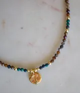 Collar corto de cuentas facetadas de crisocola y pietersita en tonos tierra, azul y verde, con esferas doradas intercaladas y un dije redondo dorado con diseño de estrellas y pequeños cristales.