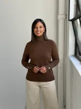 Polera de tejido de punto color chocolate, con cuello alto y mangas largas que presentan detalles de botones dorados en los puños.