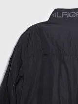 Campera bomber Tommy Hilfiger negra de poliéster, con cuello alto, cierre frontal con cremallera, dos bolsillos laterales con cremallera, puños elásticos y logo bordado en el pecho.