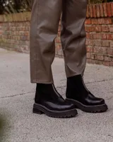 Botinetas de cuero negro con diseño combinado en gamuza y cuero texturizado. Presentan cierre frontal central, suela track dentada con costuras visibles en contraste y caña media.