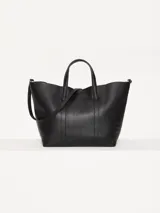 Cartera tipo tote Jazmín Chebar de cuero vacuno negro, con manijas superiores, correa regulable extraíble, acceso mediante imán y punteras metálicas decorativas.