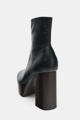 Botín de caña baja con cierre lateral mediante cremallera. Presenta un diseño de punta redonda con cuerpo de cuero negro y suela de plataforma con tacón alto de bloque con acabado efecto madera.
