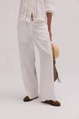 Pantalón de lino lavado color beige, de calce recto y diseño relajado. Presenta cintas de lino desflecadas aplicadas en los laterales con pespunte central, pretina con botón metálico, bolsillos delanteros y traseros.