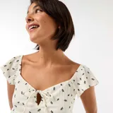 Top de tejido arrugado color blanco con estampado floral oscuro, escote cuadrado con pequeño lazo y recorte frontal, y mangas cortas con volados.