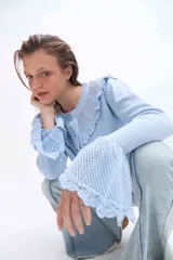 Saco de punto color celeste, con cuello redondo y mangas largas con puños acampanados de encaje tejido. Cuenta con cierre frontal de botones.