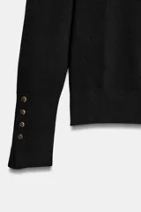 Jersey de punto liso en color beige, con cuello alto y manga larga con detalle de botones metálicos en los puños.