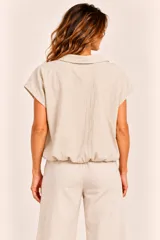 Camisa de manga corta color beige, con cuello camisero, cierre frontal de botones y ruedo con elástico ajustado.