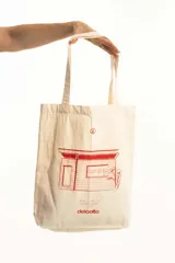 Bolso tipo totebag de tela color crudo con estampa de una casa en color rojo.