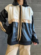 Campera con cuerpo de corderito color beige, mangas y parte inferior de cuero sintético negro con textura tipo cocodrilo. Tiene cuello estilo camisa con solapas de corderito negro, cierre frontal con cremallera y bolsillos laterales.