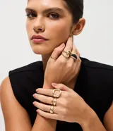 Kit de seis anillos de diseño variado con acabado en tono dorado claro. Incluye piezas de metal con texturas lisas, torcidas y caladas, además de un anillo con detalle de resina negra. Diseñados para ser usados en conjunto o por separado.
