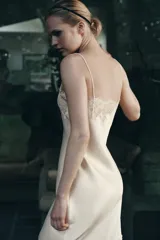 Vestido midi de estilo lencero confeccionado en tejido satinado color beige. Presenta escote recto con tirantes finos y aplicaciones de encaje a tono en el escote y en el ruedo.